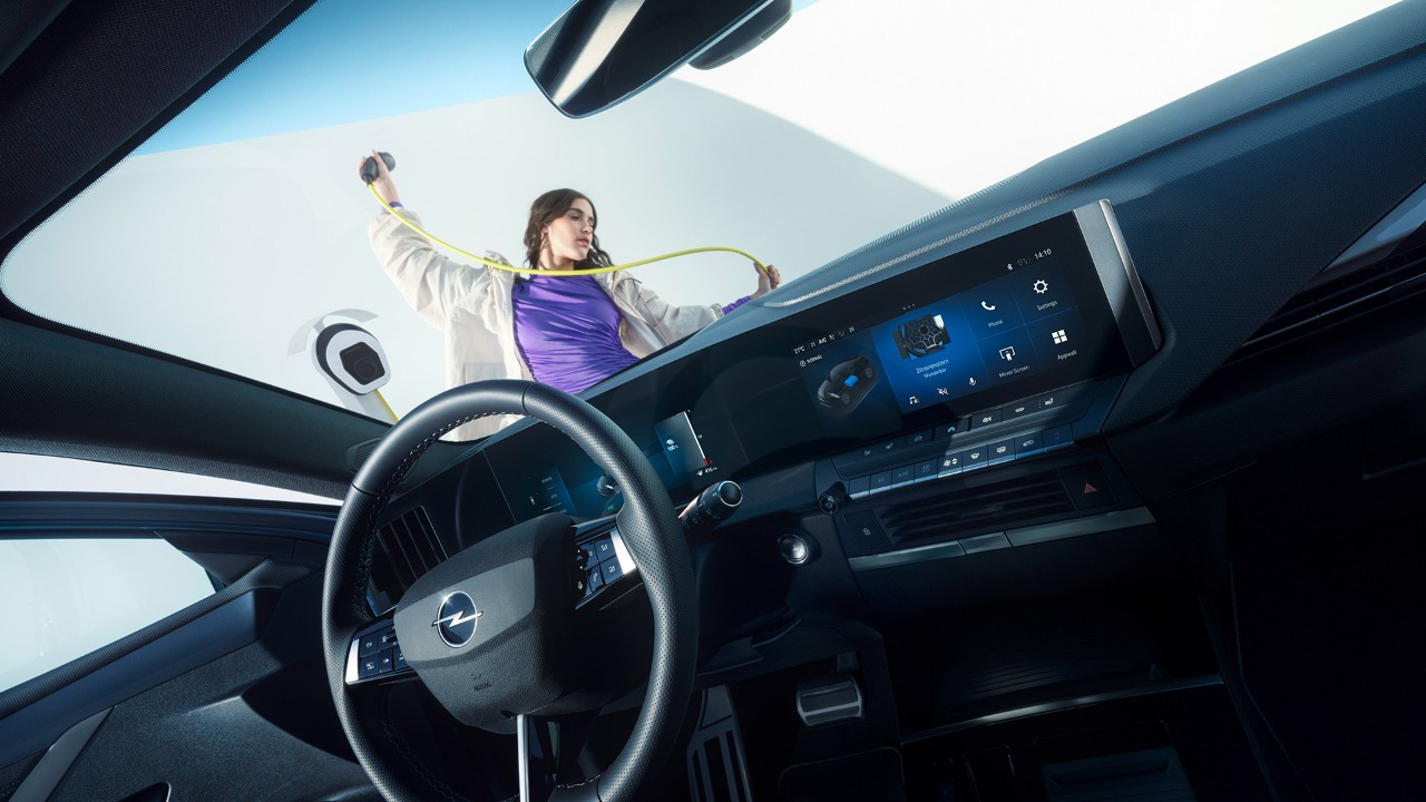 Egy Opel Astra Electric belső nézete az utasülésről, miközben egy nő töltőkábelt tart kint