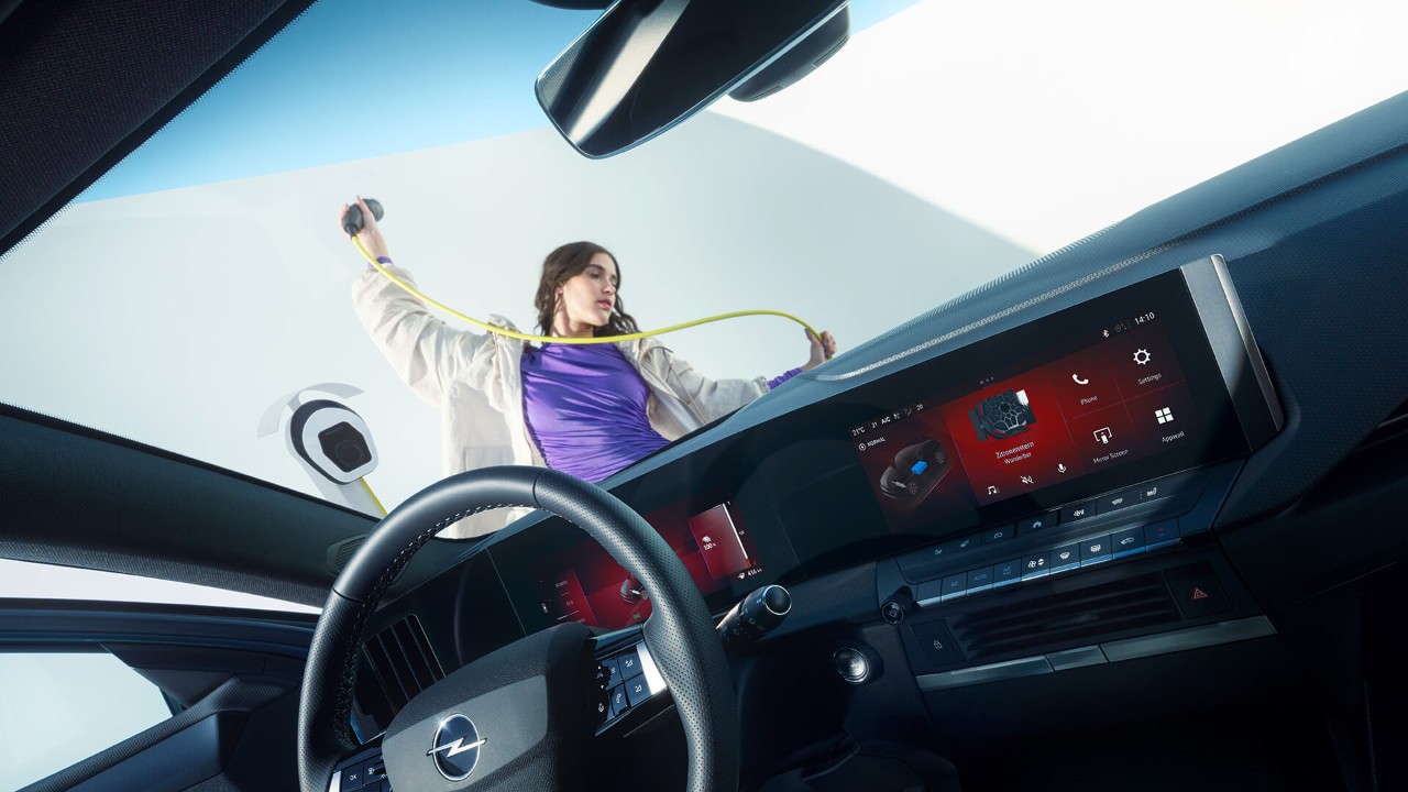 Közelkép egy Opel Astra Sports Tourer Electric belsejéből, kint egy nő elektromos töltőkábelt tart a kezében