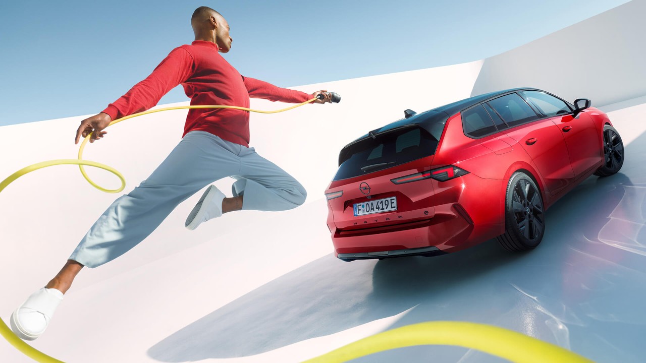 Egy férfi a levegőbe ugrik egy elektromos töltőkábellel, háttérben egy Opel Astra Sports Tourer Electric modellel