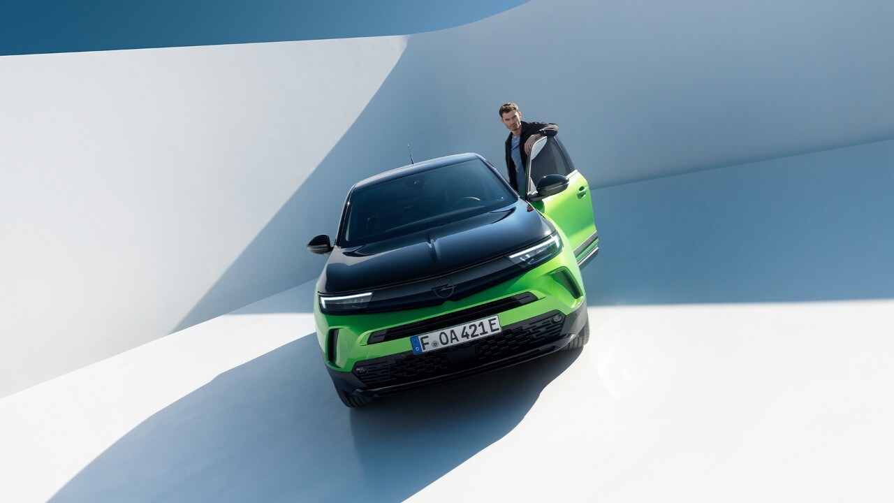 Front view of a green Opel Mokka Electric with black alloys and roof with a man getting in from the driver's door