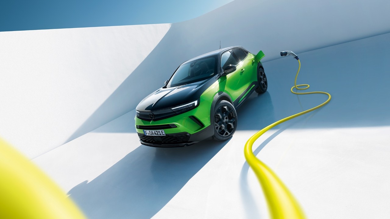 Front side view of a green Opel Mokka Electric with black alloys and roof with a yellow EV charging cable